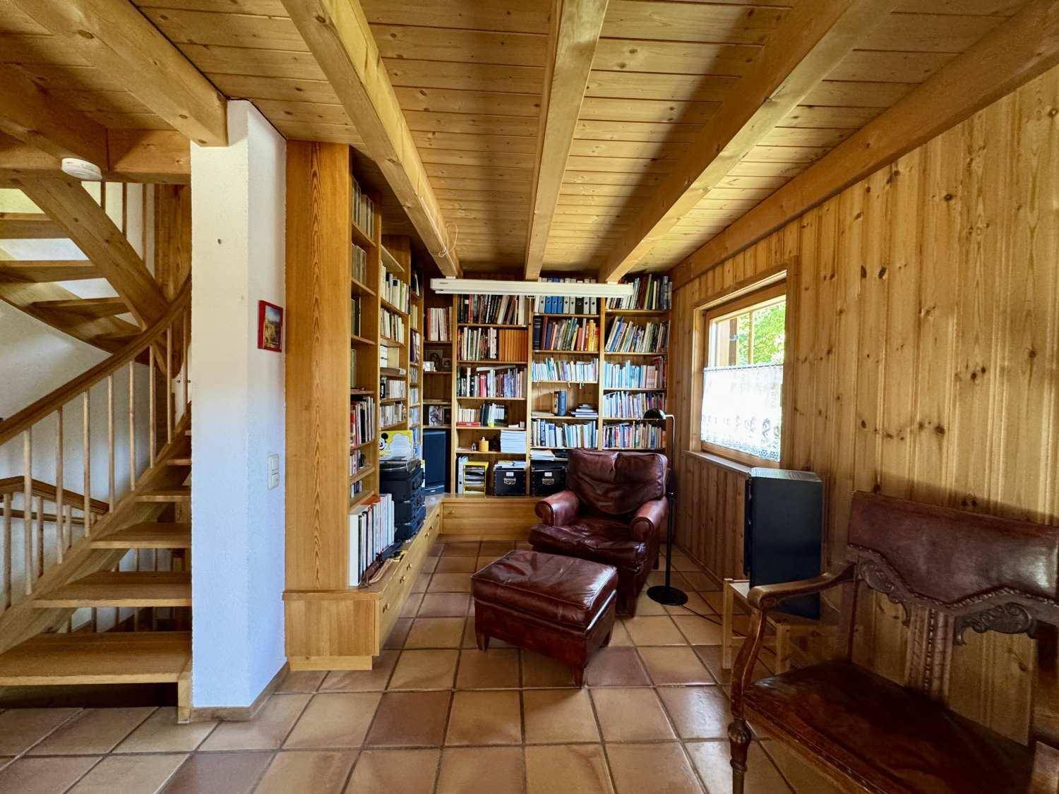 Helles Arbeitszimmer mit Holzbalkendecke, Bücherregalen und Terrakottafliesen.