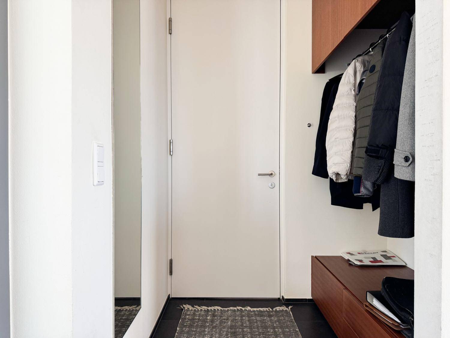 Heller Eingangsbereich mit Garderobe, Spiegel und dunklem Fliesenboden.