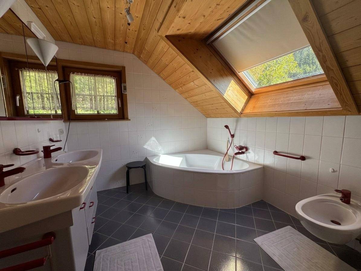 Badezimmer im Dachgeschoss mit Eckbadewanne, Doppelwaschbecken und Dachfenster.