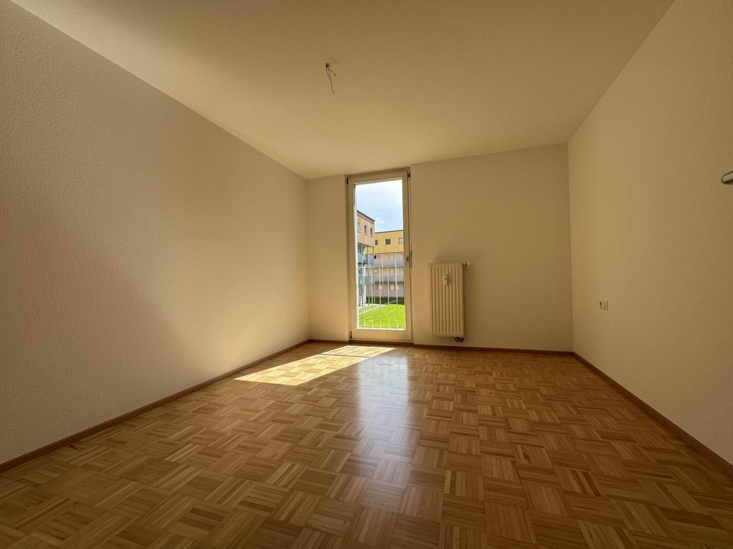 Sonniger Raum mit Parkettboden und großem Fenster, ideal als Schlaf- oder Kinderzimmer.