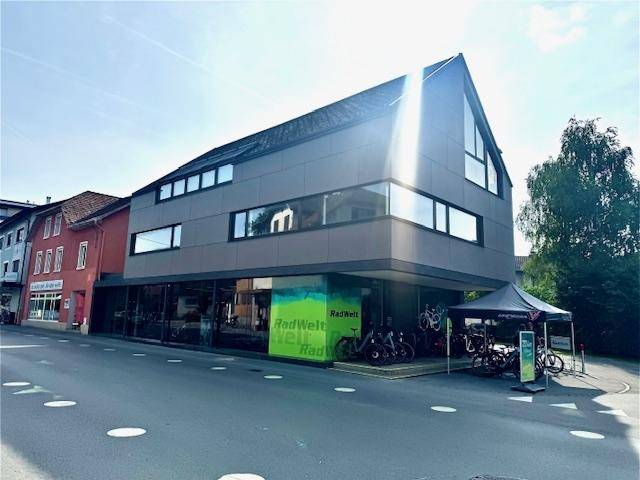 Modernes Geschäftsgebäude mit markanter Architektur, großen Fenstern und einer Fahrradhandlung im Erdgeschoss.
