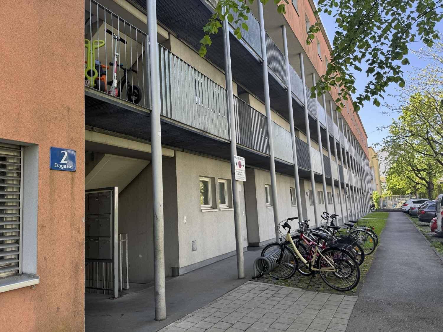 Eingangsbereich eines Wohngebäudes mit Fahrradständern und Balkonen an einem sonnigen Tag.