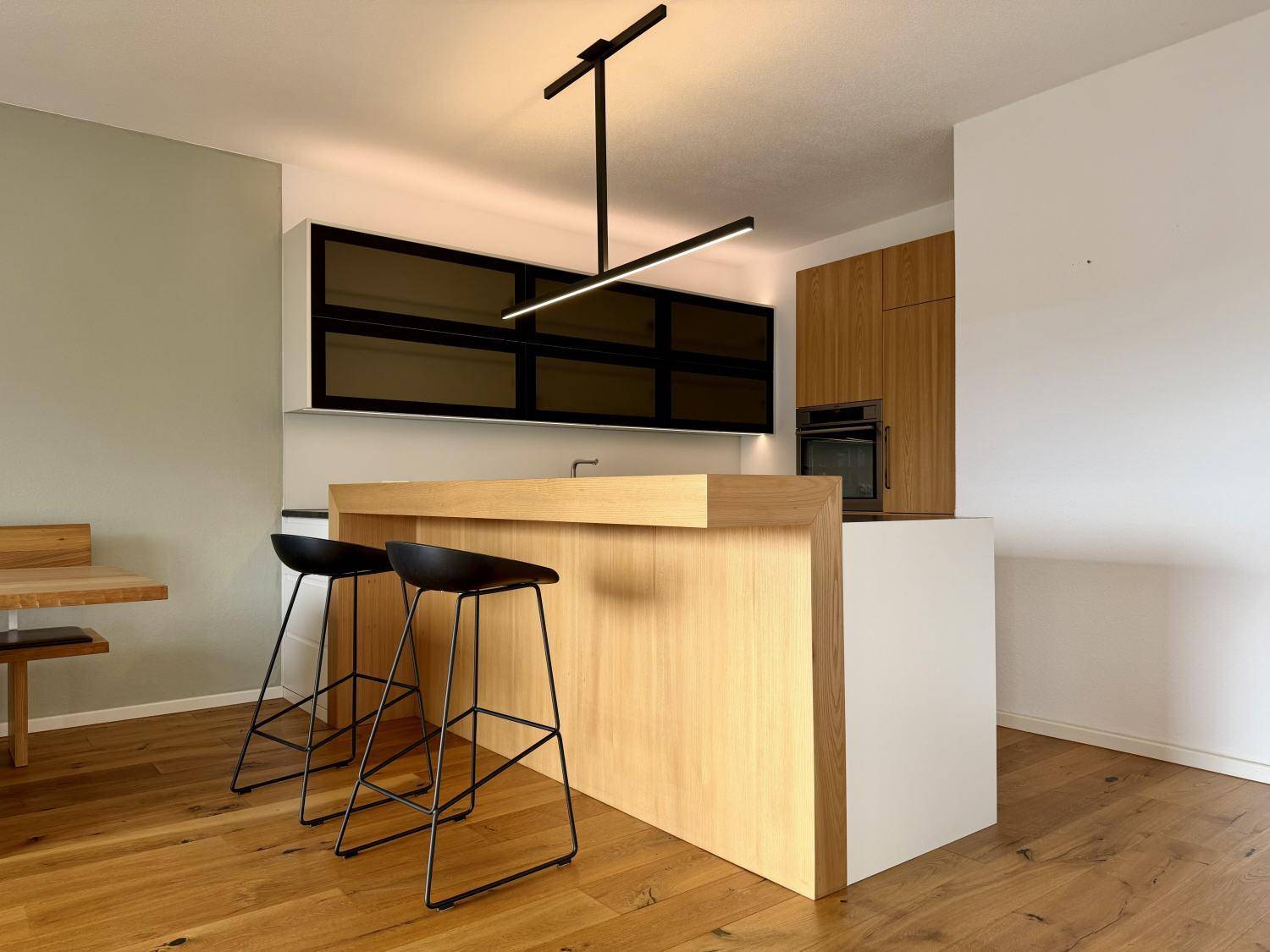 Moderne Küche mit Holzinsel, weißen Schränken, Barhockern und stilvoller Beleuchtung.