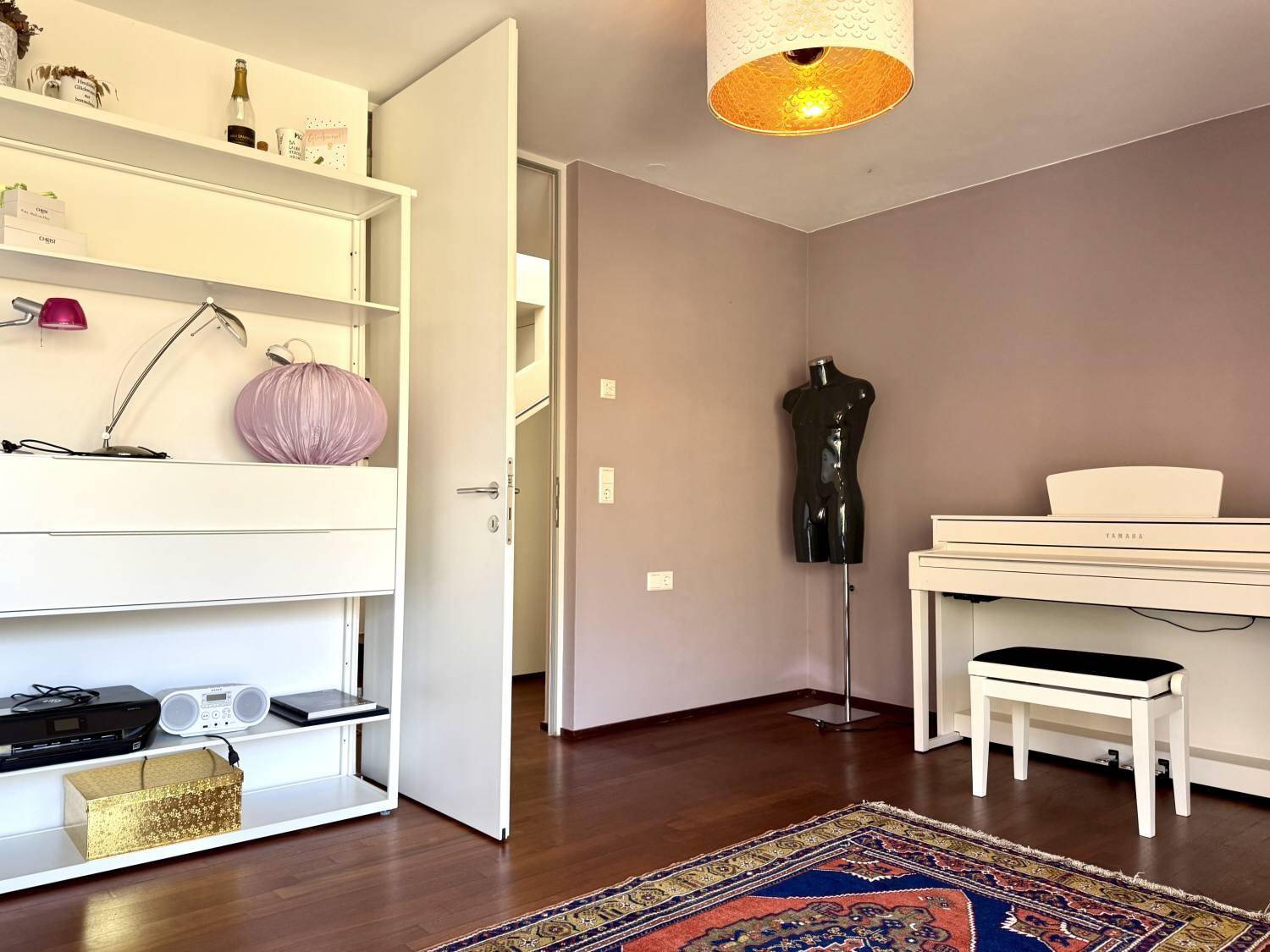 Zimmer mit Klavier, Regal und Holzboden, vielseitig nutzbar als Schlaf- oder Arbeitszimmer.