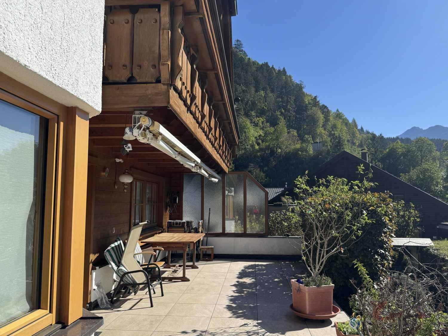 Sonniger Terrassenbereich mit Fliesenboden, Gartenmöbeln und Blick auf die Berge.