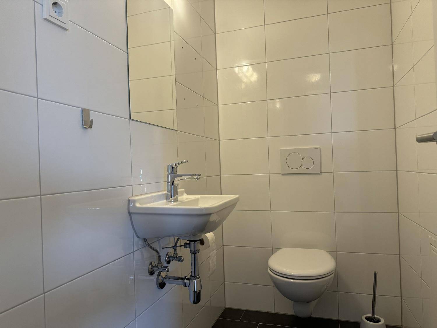 Kleines, hell gefliestes Badezimmer mit wandmontierter Toilette, Waschbecken und Spiegel.