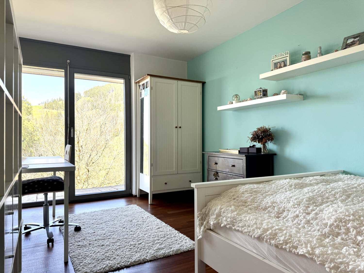 Kinderzimmer mit Einzelbett, Schreibtisch und Zugang zum Balkon mit grüner Aussicht.