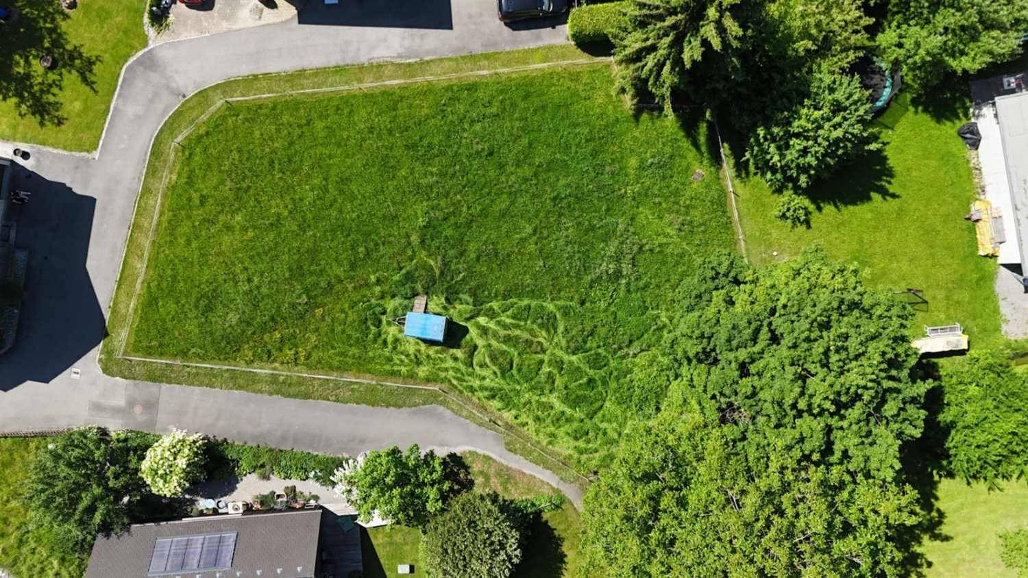 Grünes Grundstück aus der Vogelperspektive mit angrenzenden Straßen und Bäumen.