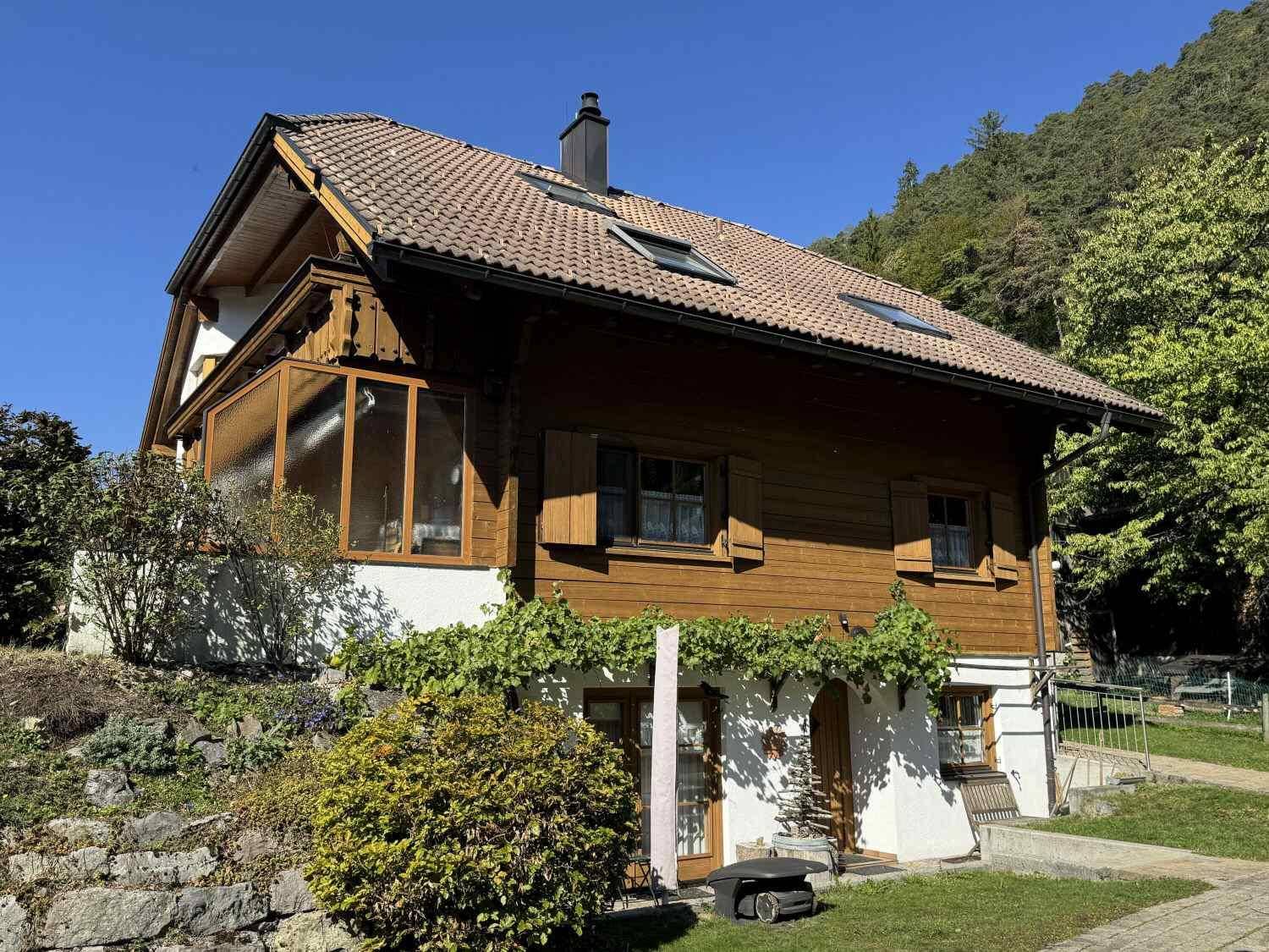 Rückansicht des Hauses mit Holzfassade, Fensterläden und einem verglasten Wintergarten.
