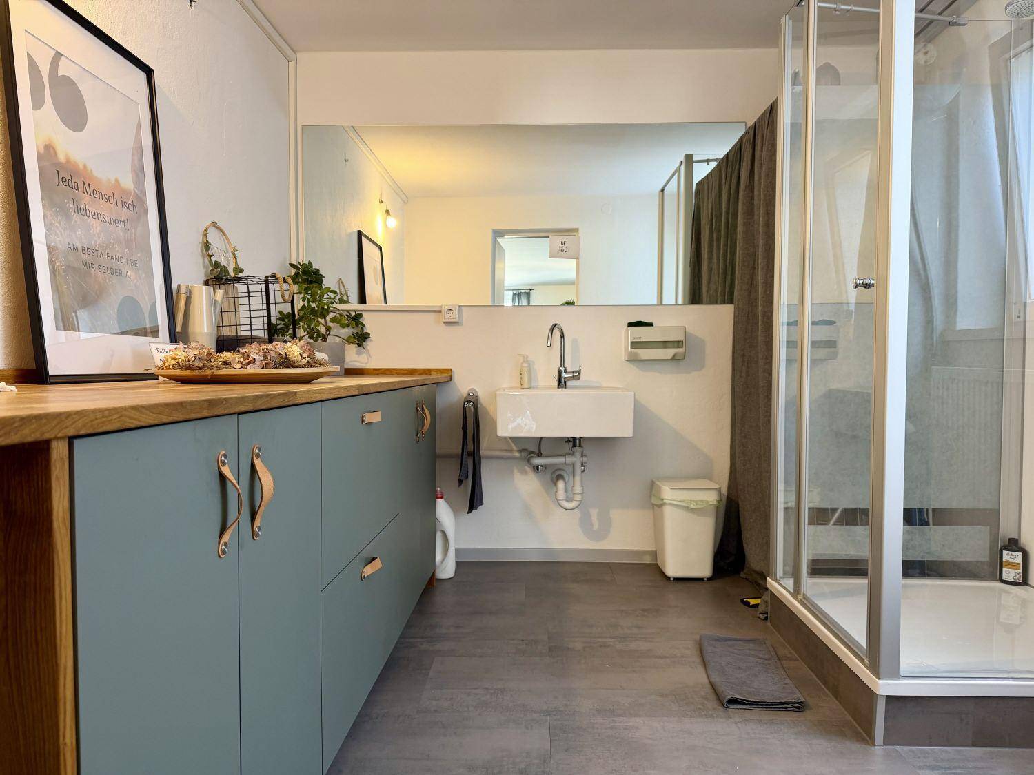 Modernes Badezimmer mit Waschtisch, großem Spiegel und einer Duschkabine, passend zum Design des Studios.