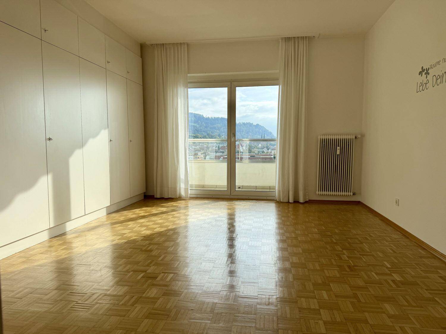 Schlafzimmer mit Parkettboden, Einbauschränken und Balkonzugang mit Bergblick.