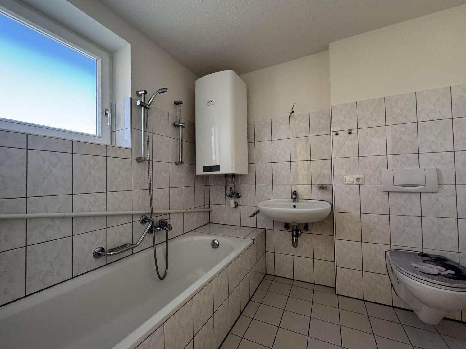 Gefliestes Badezimmer mit Badewanne, Waschbecken, WC und Fenster für Tageslicht.