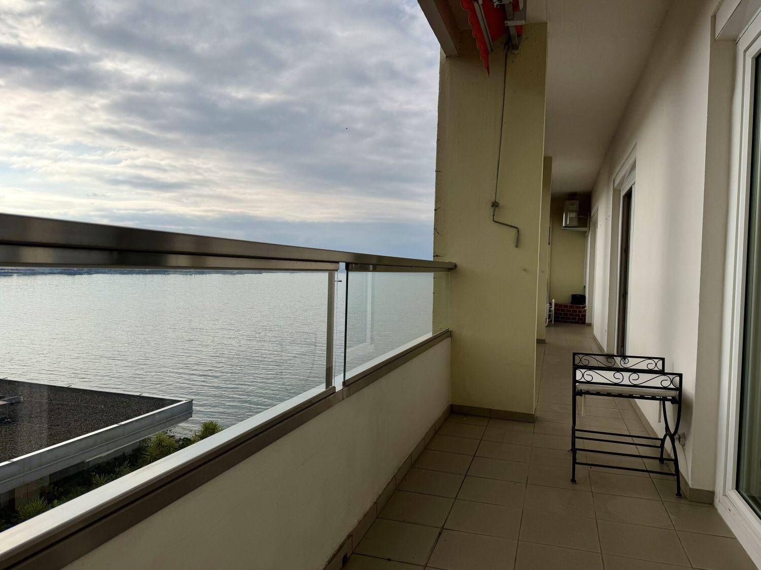 Langer Balkon mit Fliesenboden, Glasgeländer und direktem Seeblick.