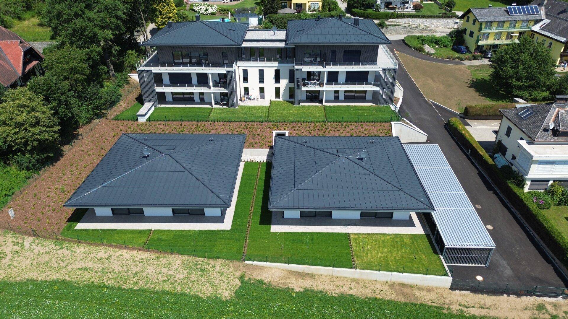 Luftaufnahme einer modernen Wohnanlage mit Hauptgebäuden und Bungalows, umgeben von Grünflächen und Zufahrten.