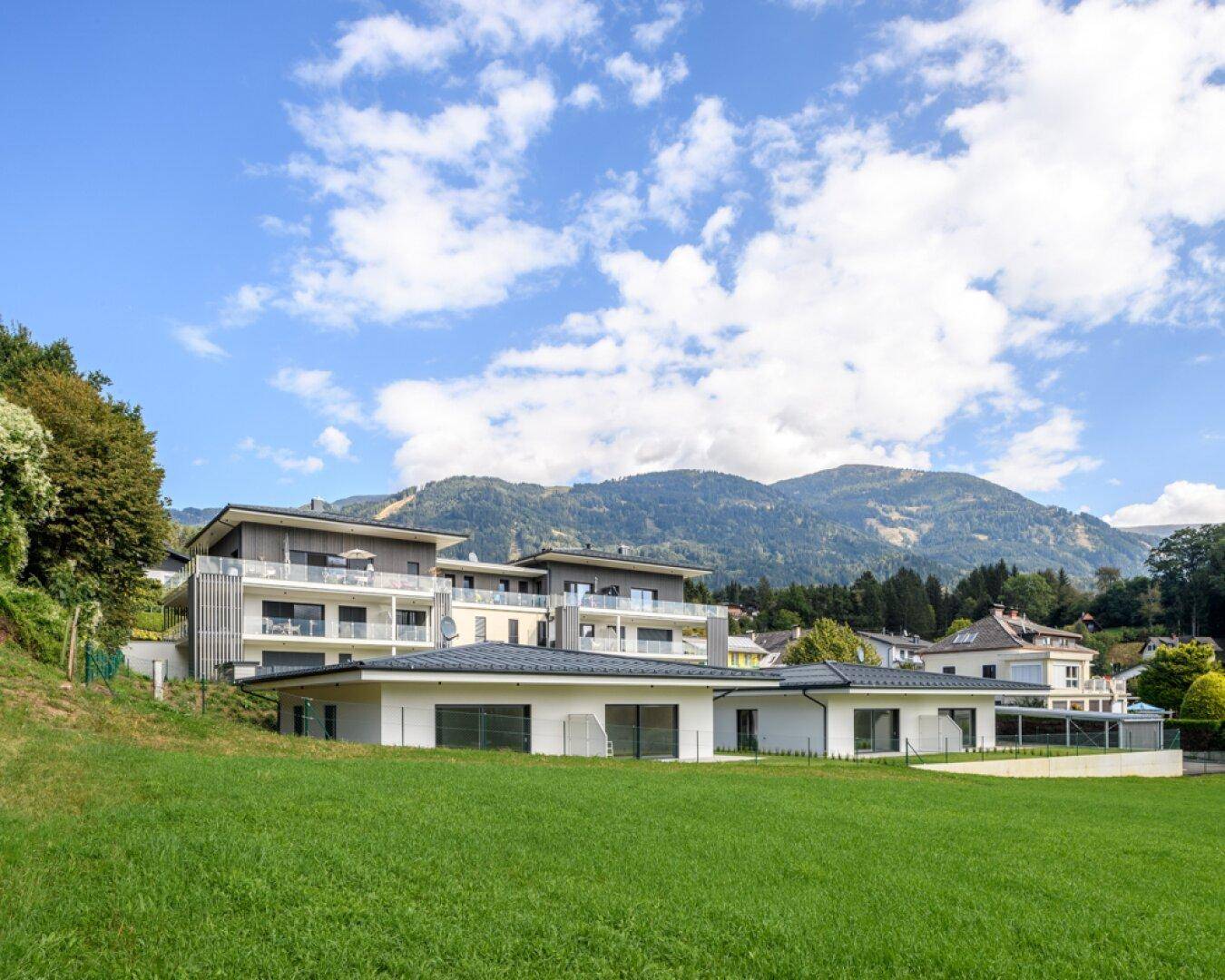 Gesamtansicht der modernen Wohnanlage mit Hauptgebäuden und Bungalows, eingebettet in eine grüne Hügellandschaft.