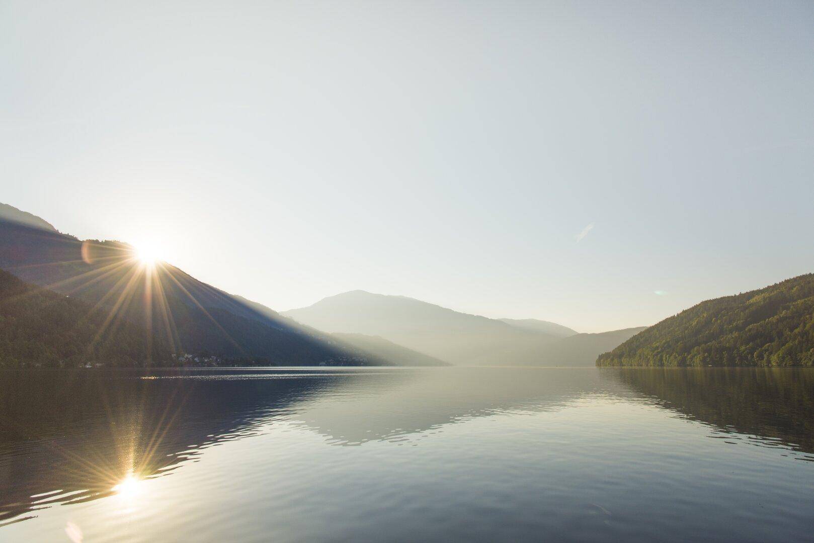Sonnenaufgang über einem ruhigen See, umgeben von majestätischen Bergen.