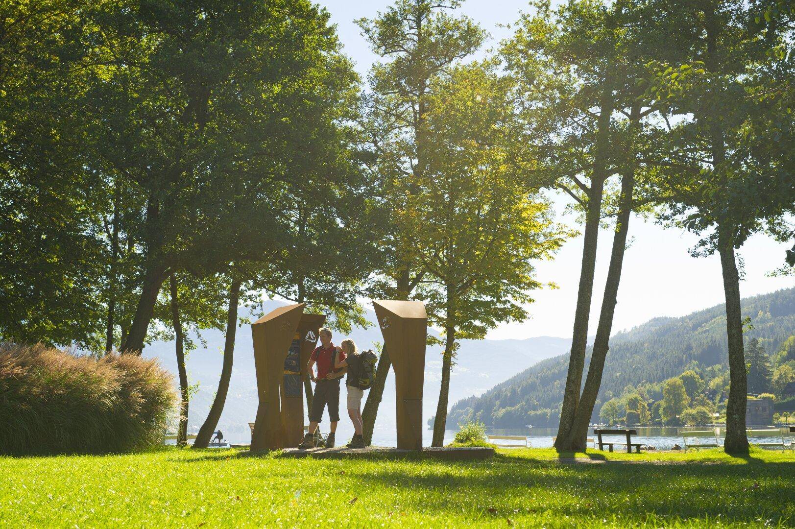 Gruppe von Menschen genießt die Natur am Seeufer mit Bäumen und Bergen im Hintergrund.
