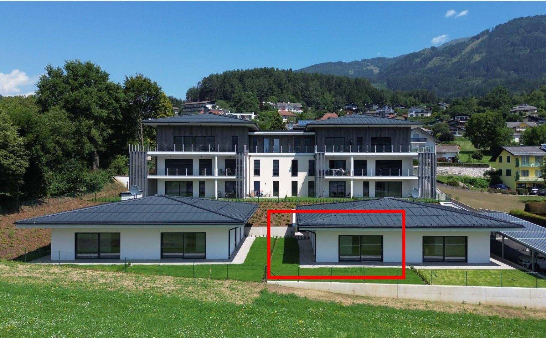 Luftaufnahme eines modernen Wohnkomplexes mit mehreren Gebäuden und Bergpanorama im Hintergrund.