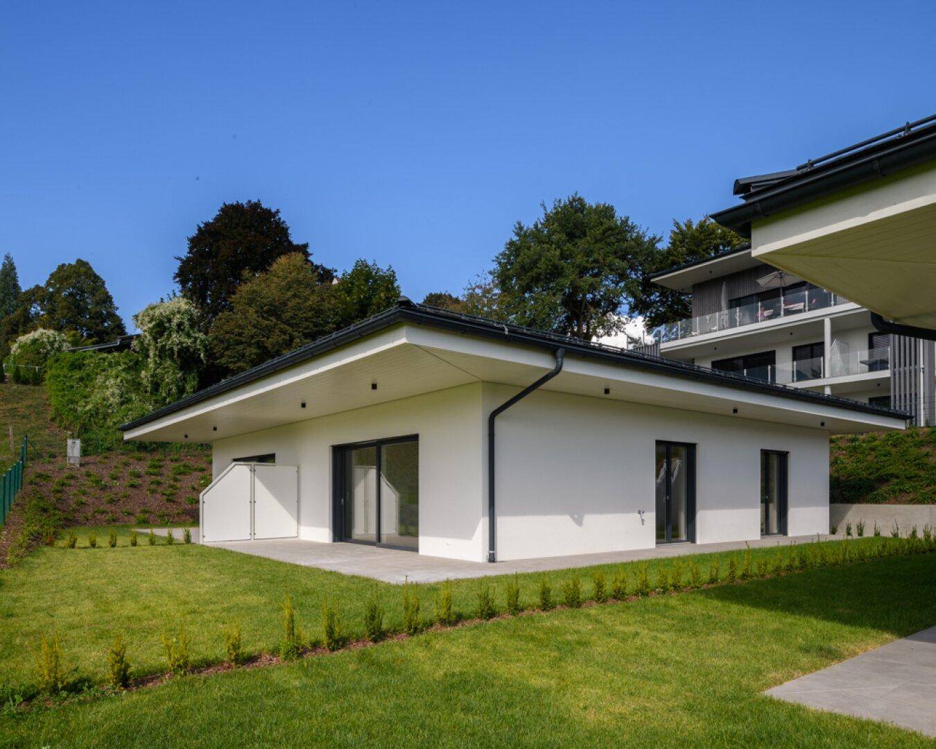 Modernes weißes Gebäude mit großen Schiebetüren und gepflegtem Rasen in einer sonnigen Landschaft.