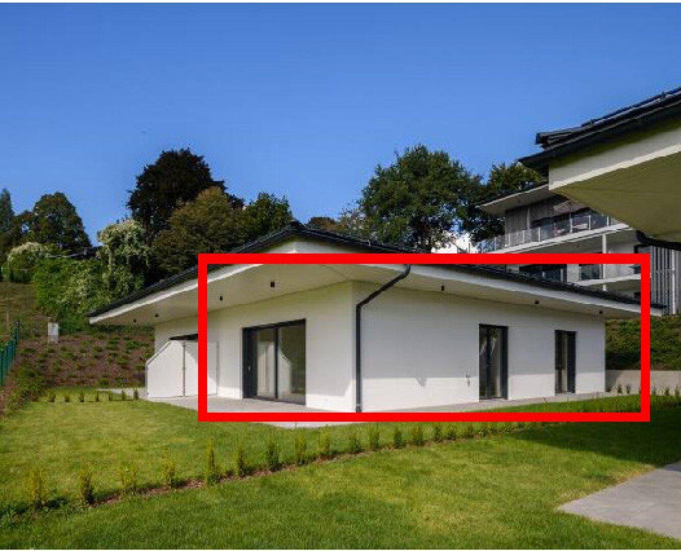 Modernes weißes Gebäude mit großen Fenstern und grüner Rasenfläche in einer hügeligen Landschaft.