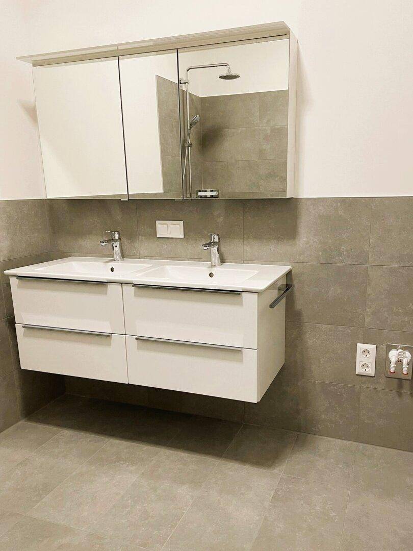 Modernes Badezimmer mit Doppelwaschbecken, Spiegelschrank und großformatigen grauen Fliesen.