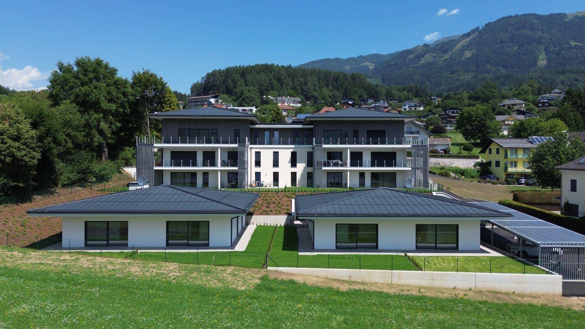 Luftaufnahme einer modernen Wohnanlage mit mehreren Gebäuden, umgeben von Natur und Bergen.
