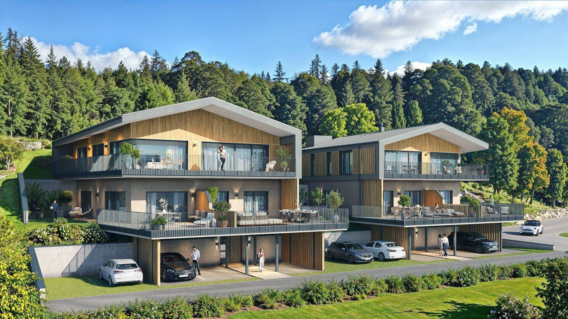 Moderne Wohngebäude mit mehreren Balkonen und Carports, eingebettet in grüne Landschaft und Berge.