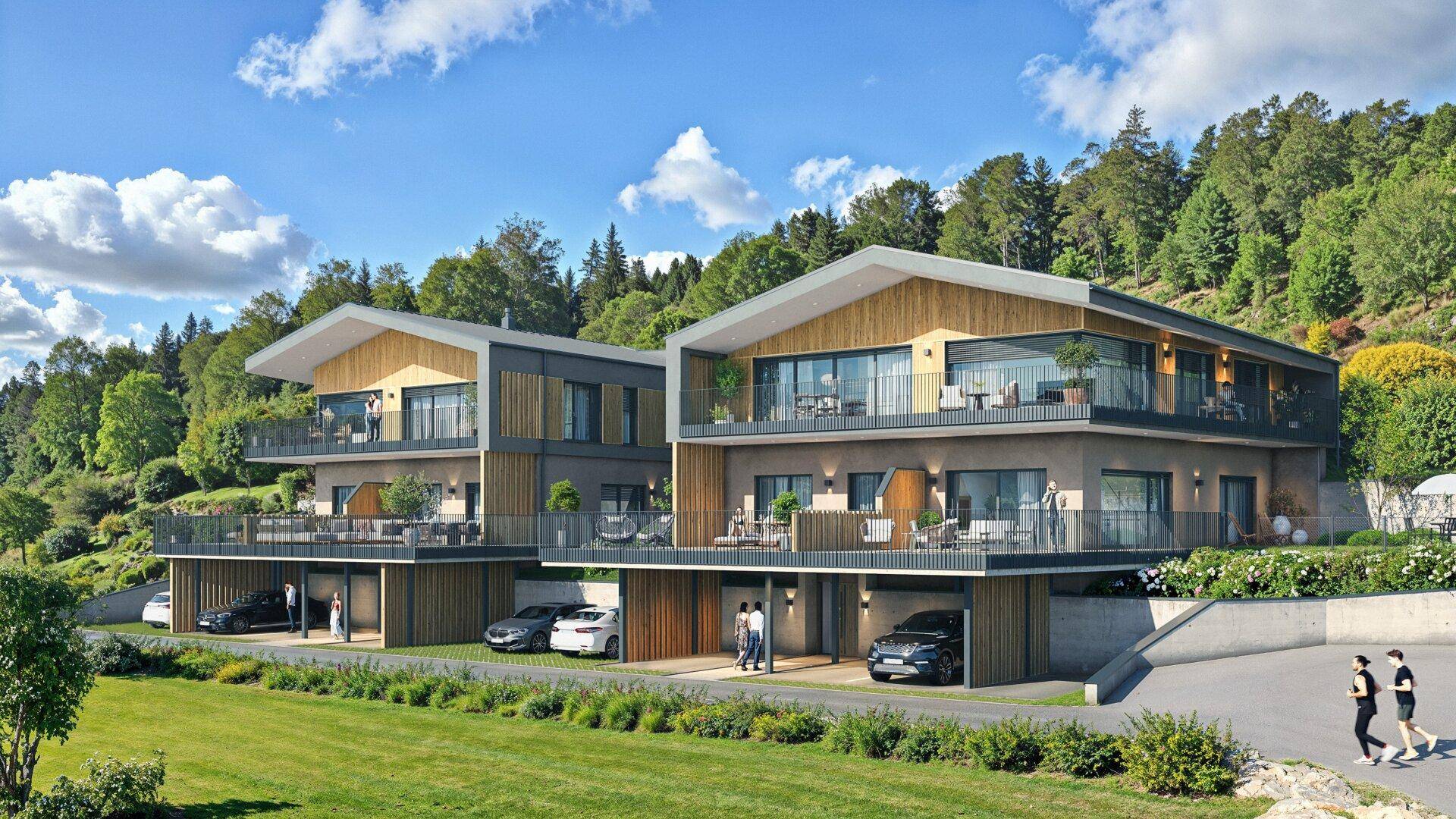 Moderne Wohngebäude mit mehreren Balkonen und Carports, eingebettet in grüne Landschaft und Berge.