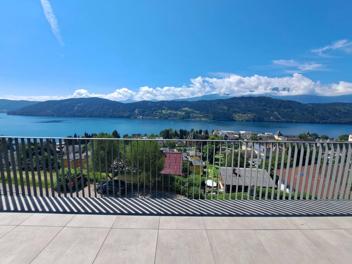 Weitläufiger Panoramablick von der Terrasse über den See, die Berge und die darunter liegende Ortschaft.
