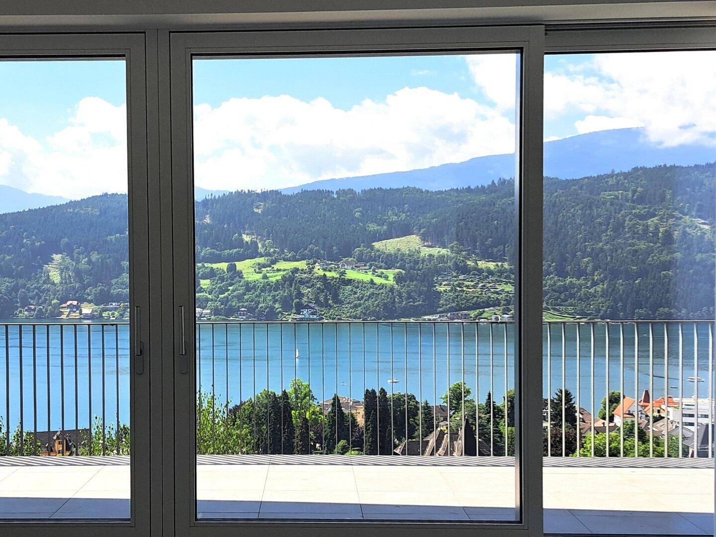 Panoramablick auf den See und die Berge durch große Fenster vom Innenbereich des Hauses.