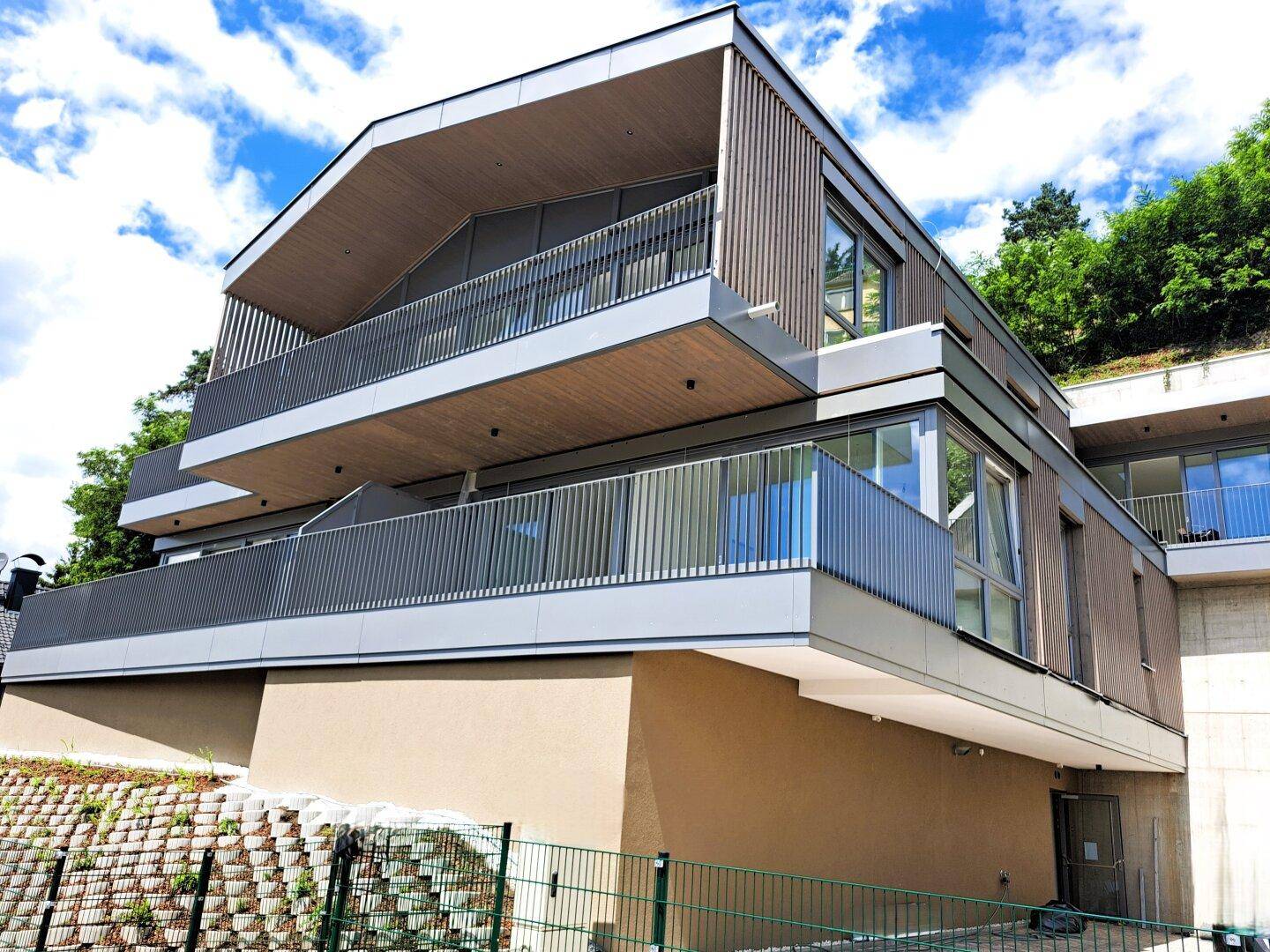 Modernes Mehrfamilienhaus mit Holzverkleidung, großen Balkonen und zeitgenössischer Architektur.