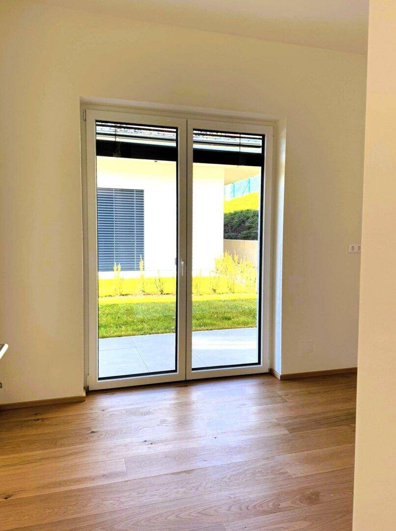 Geräumiges Zimmer mit Holzboden und Zugang zum Gartenbereich.