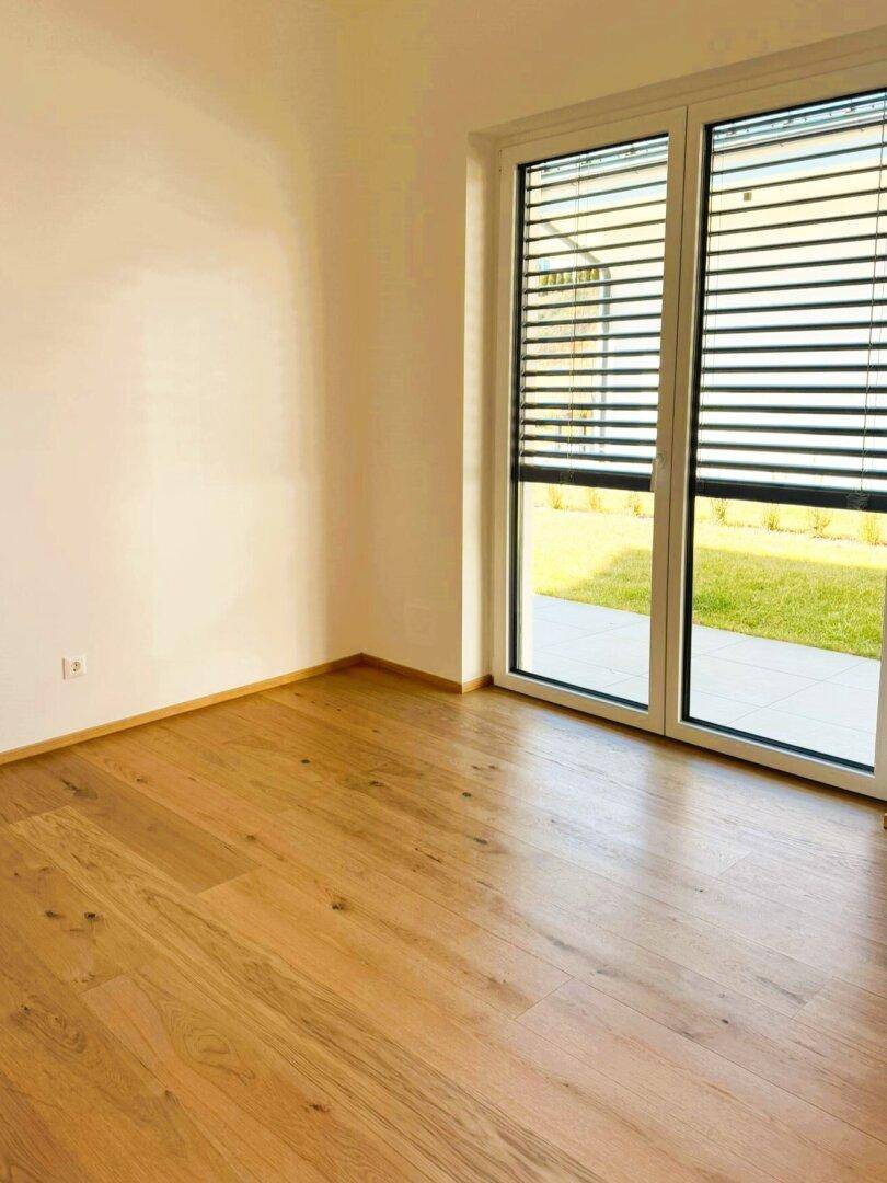 Leeres Zimmer mit Holzboden und großen Fenstern zum Garten.
