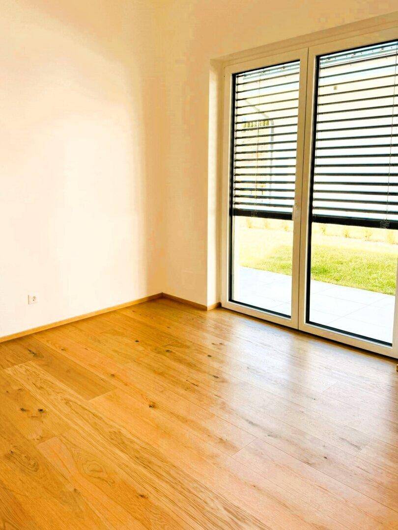 Helles Zimmer mit Holzboden und Blick auf den grünen Gartenbereich.