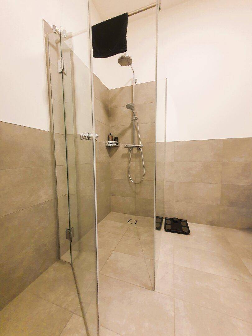 Moderne begehbare Dusche mit Glaswänden und grauen Fliesen in einem Badezimmer.