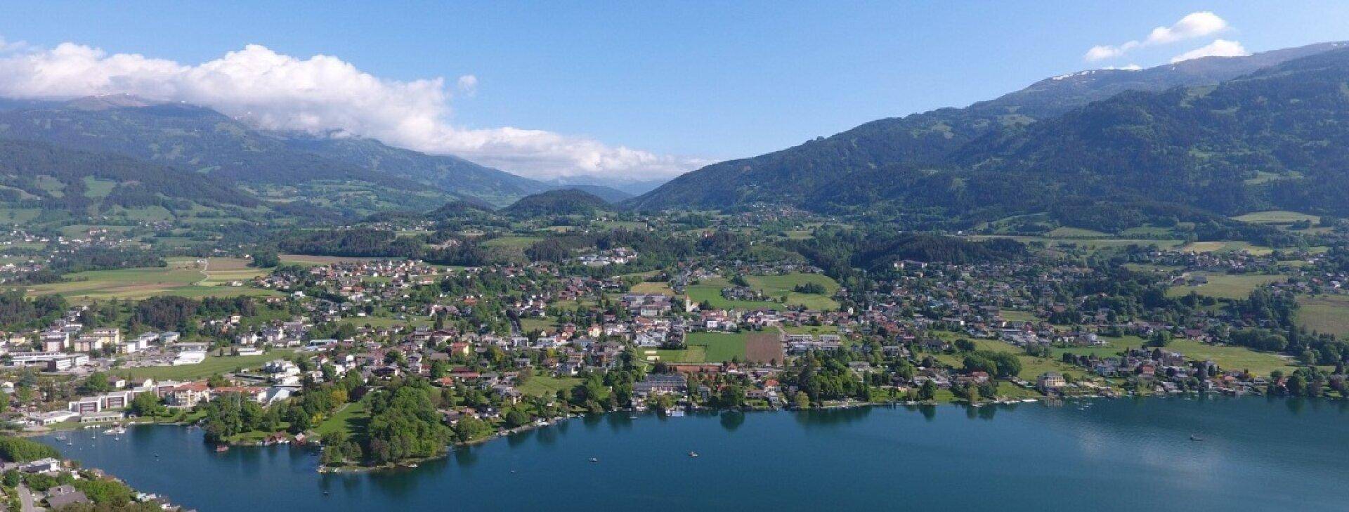 Panoramablick auf eine Stadt am See, umgeben von Bergen und grüner Landschaft.