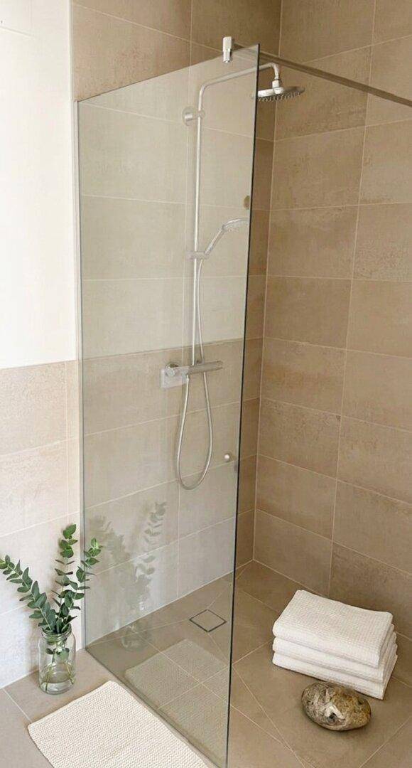 Modernes Badezimmer mit begehbarer Dusche, beigefarbenen Fliesen und minimalistischem Design.