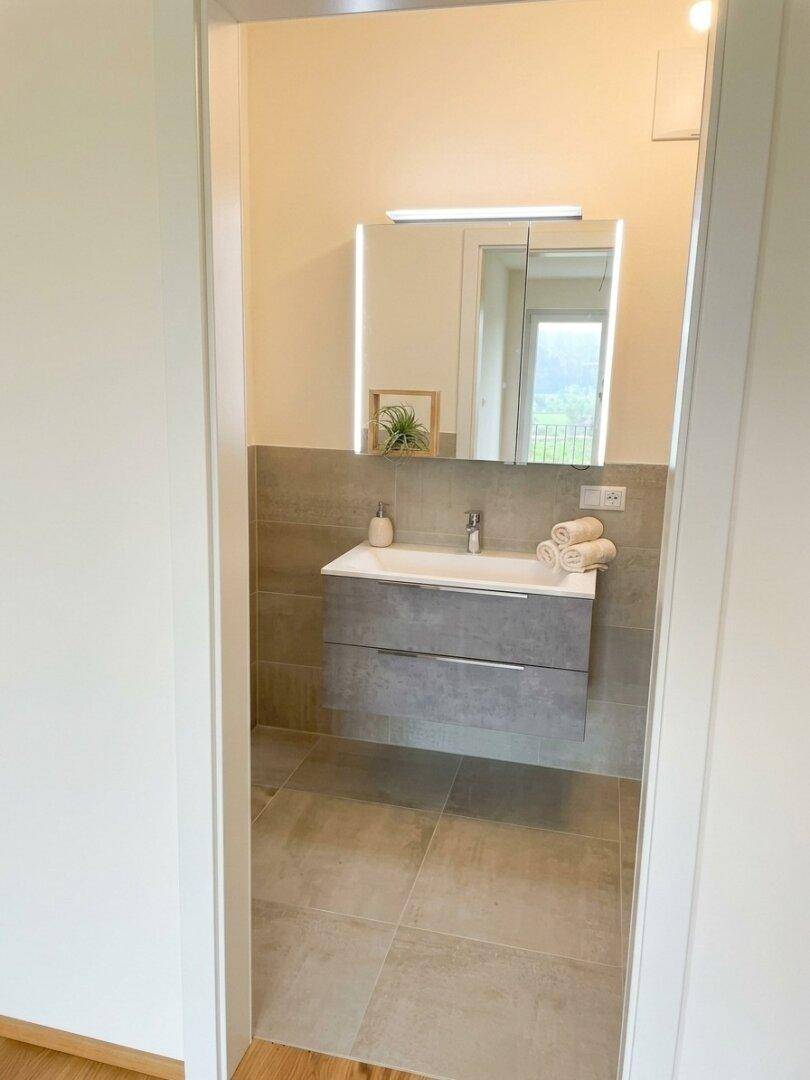 Modernes Badezimmer mit Waschtischunterschrank, beleuchtetem Spiegelschrank und Fliesenboden.
