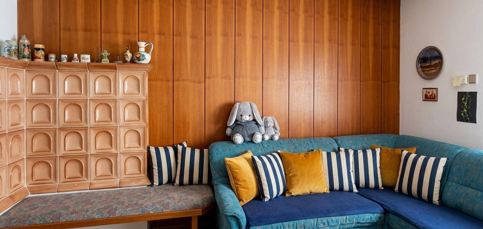Traditionelles Wohnzimmer mit Holzwänden, blauem Ecksofa und einem charakteristischen Kachelofen.