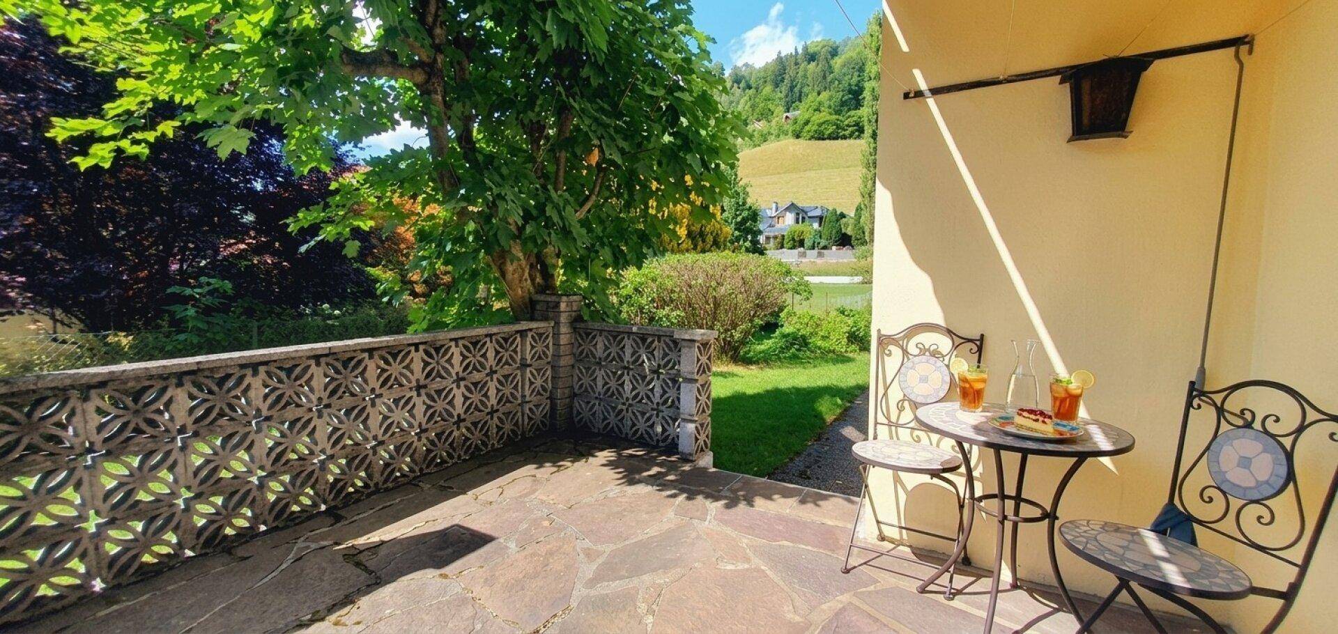 Sonniger Terrassenbereich mit Steinfliesen, schmiedeeisernen Möbeln und Blick auf grüne Hügel.