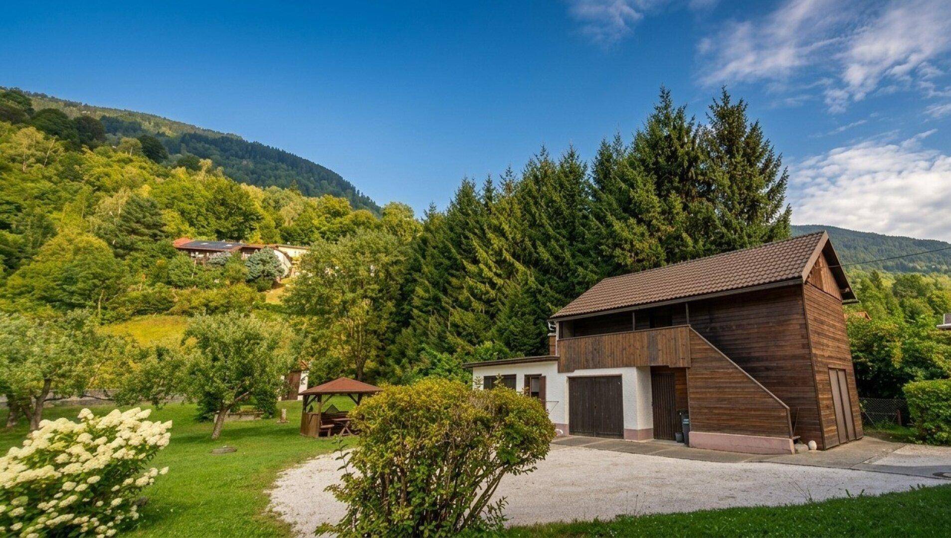 Gesamtansicht des Anwesens mit Hauptgebäude, Garagen, Garten und beeindruckender Berglandschaft.