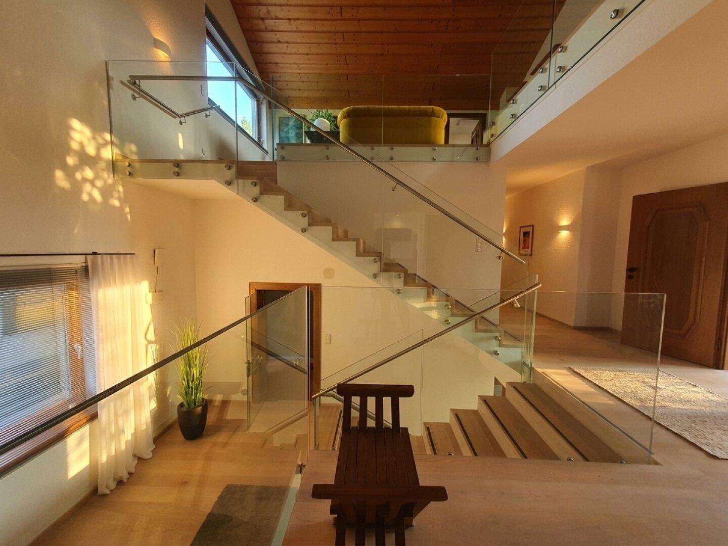 Heller Flur mit eleganter Glas-Treppe, die verschiedene Ebenen des Hauses verbindet.