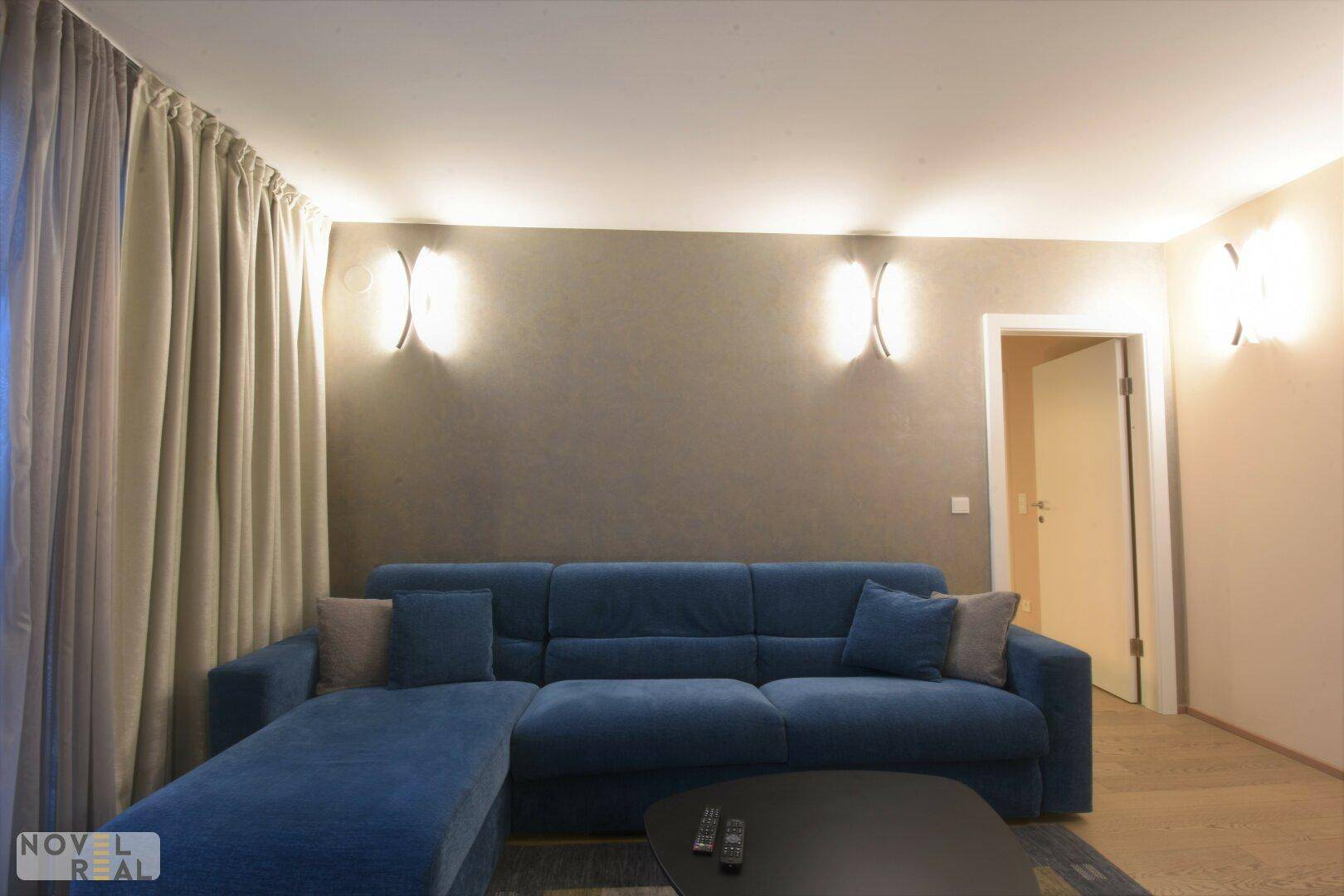 Modernes Wohnzimmer mit blauer Eckcouch, Wandleuchten und hellem Parkettboden.