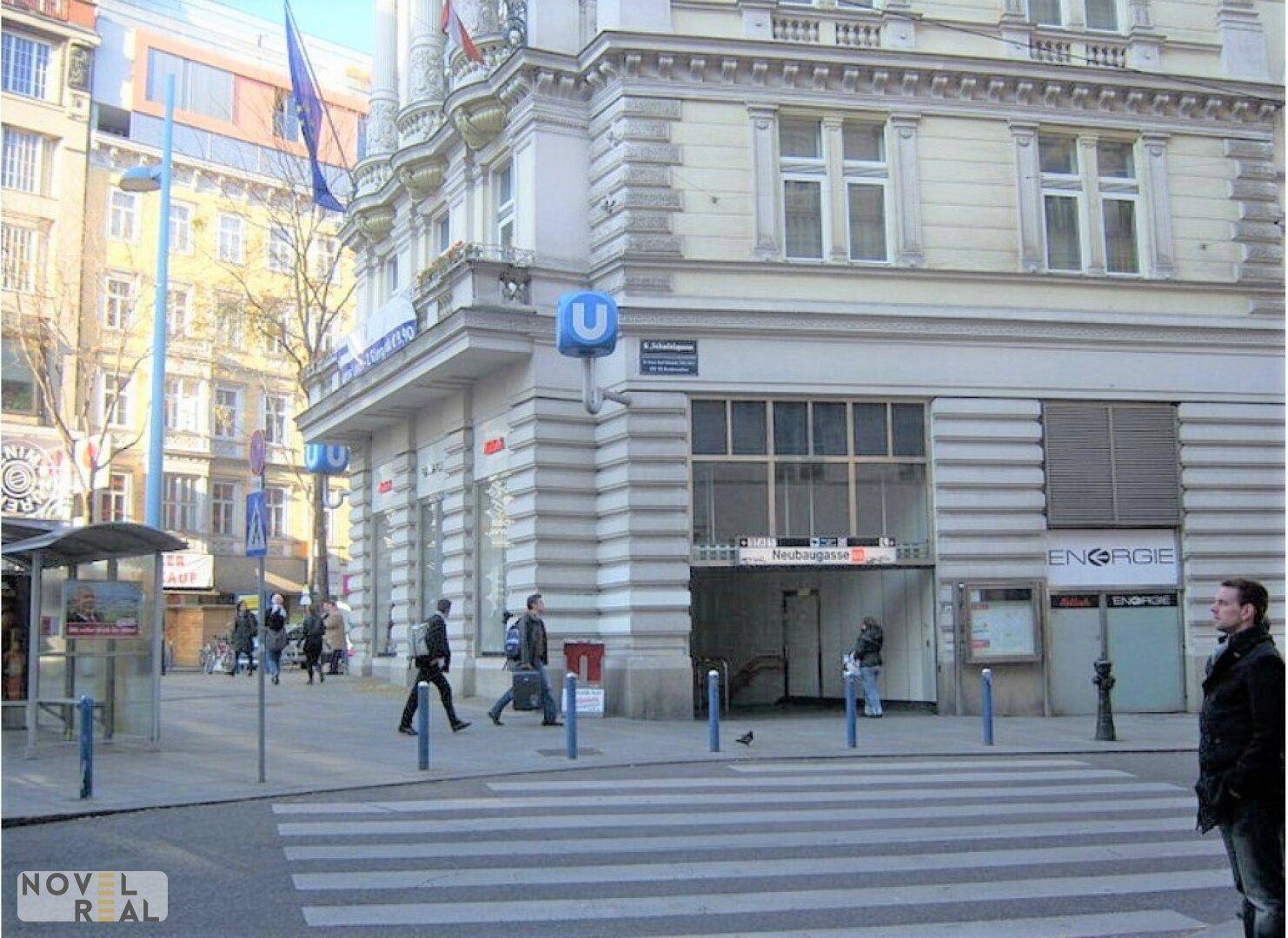 Belebte Straßenszene mit U-Bahn-Eingang und historischer Gebäudefassade in urbaner Umgebung.