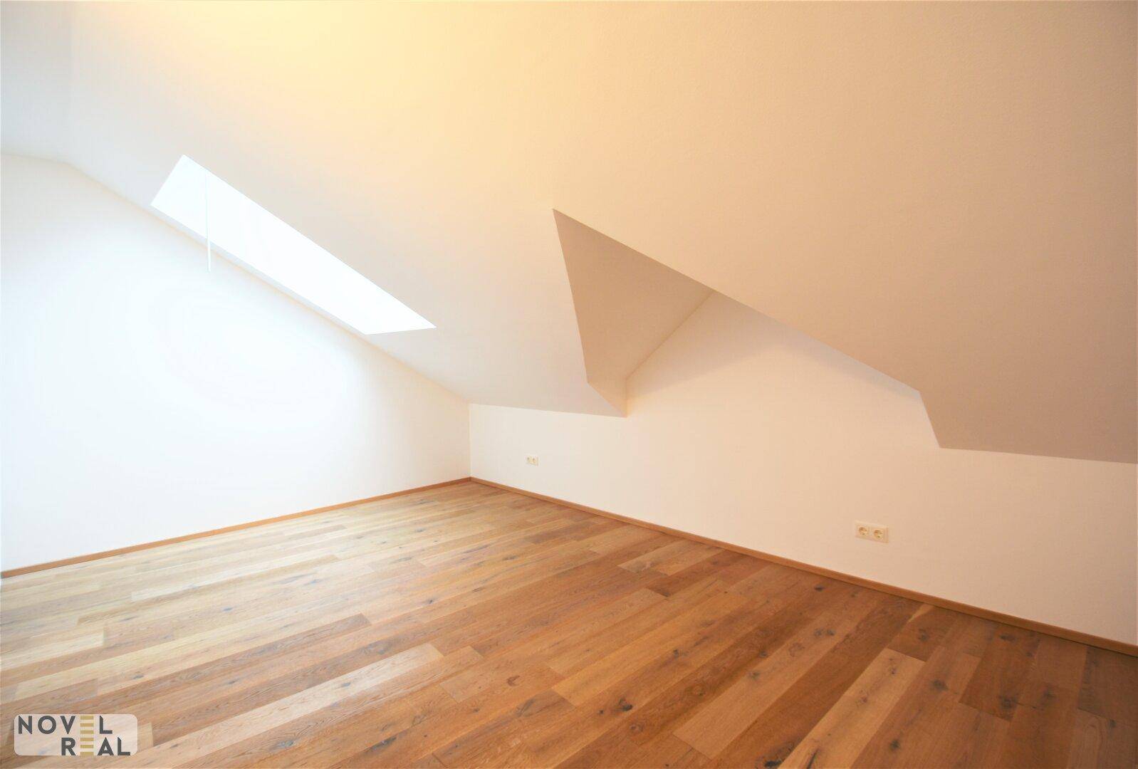 Helles Zimmer mit Holzboden, Dachschräge und Dachfenster für viel Tageslicht.