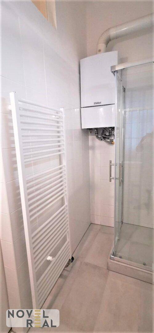 Badezimmer mit Duschkabine, Handtuchheizkörper und Gastherme an der Wand.