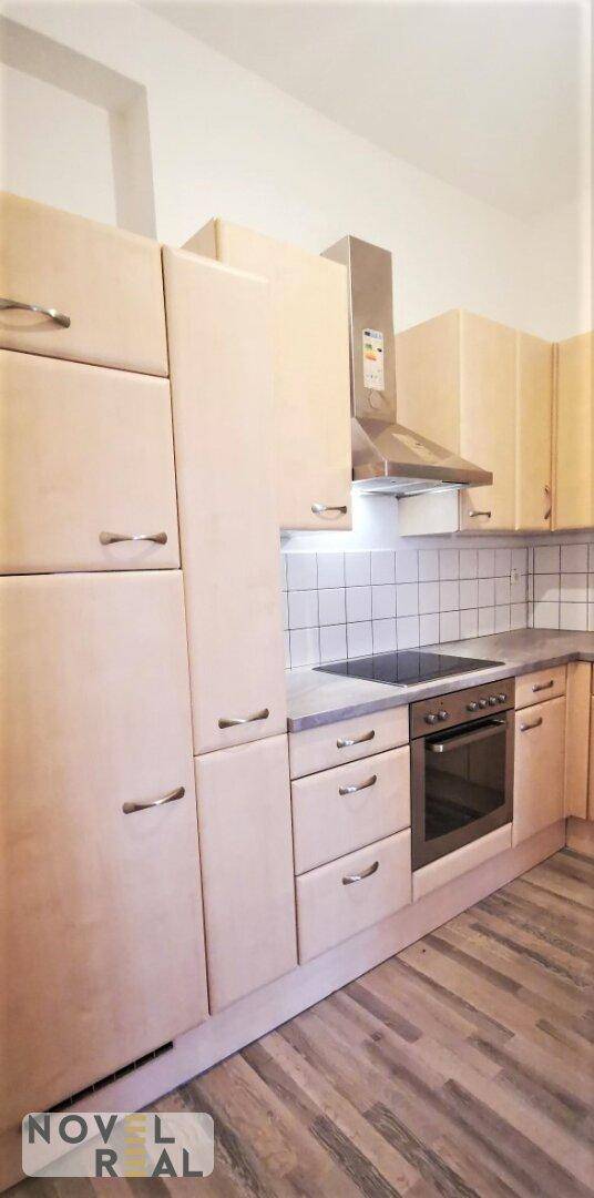 Helle Einbauküche mit Holzfronten, Kochfeld und Dunstabzugshaube in gutem Zustand.