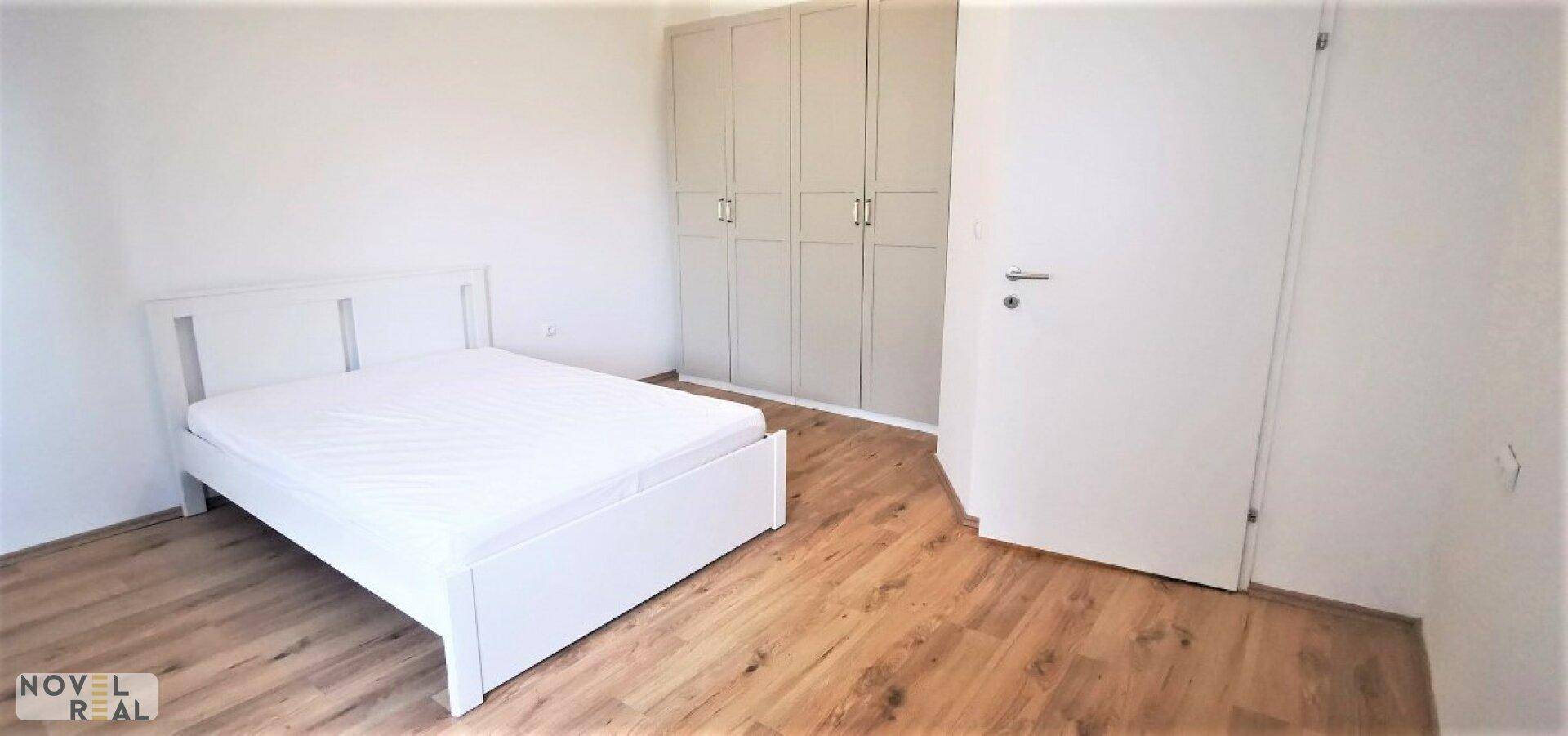 Schlafzimmer mit weißem Bettgestell, Kleiderschrank und Laminatboden.