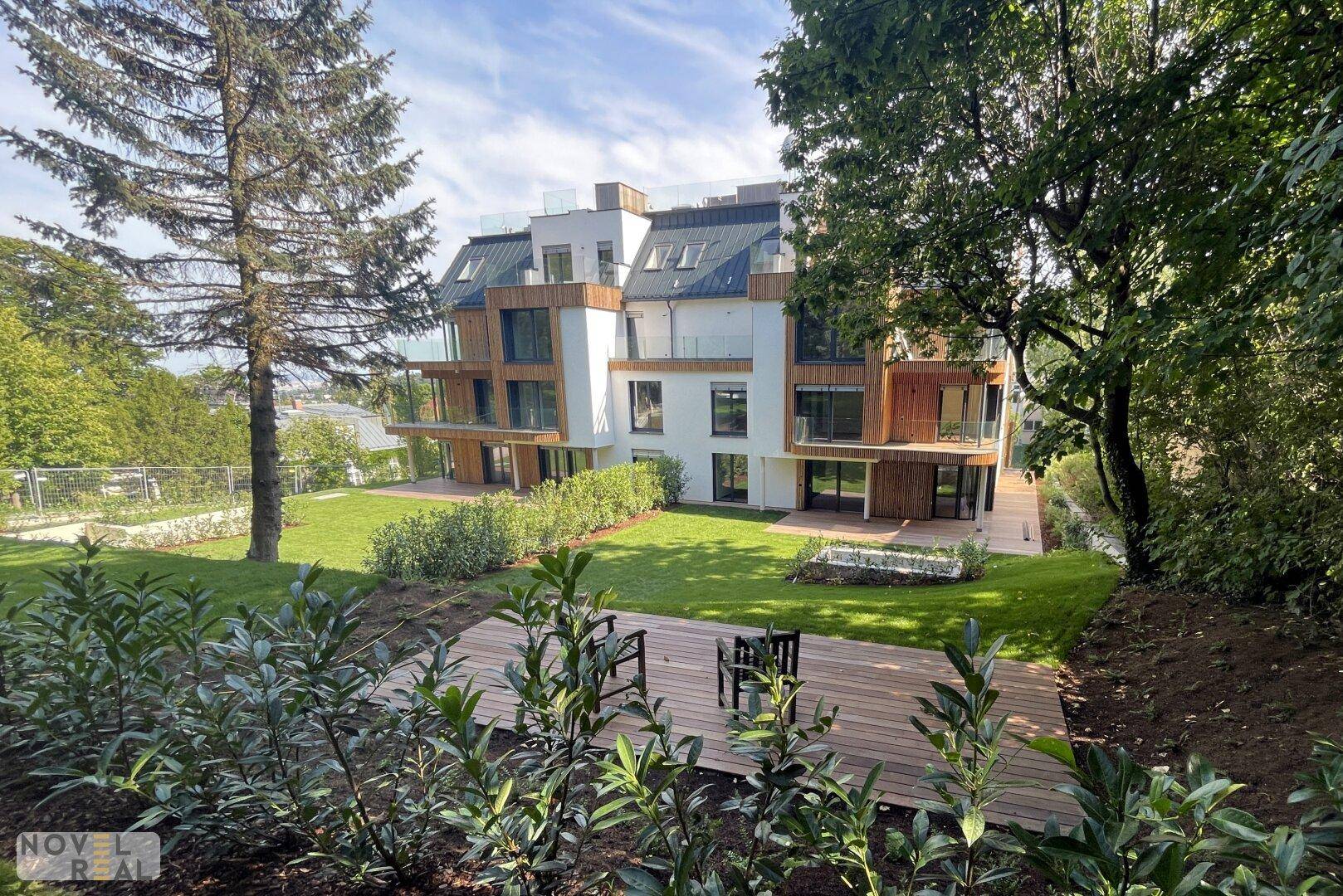 Rückansicht eines modernen Gebäudes mit gepflegtem Garten, Rasenflächen und Holzterrassen.