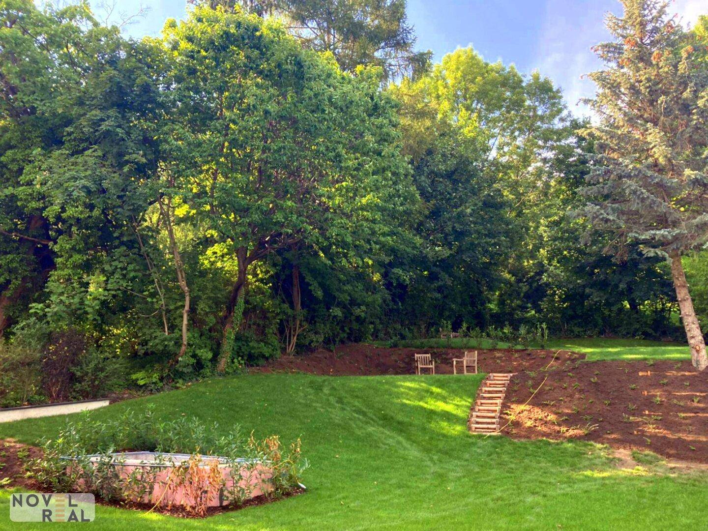 Großer, gepflegter Gartenbereich mit üppiger Vegetation, Rasenflächen und Sitzgelegenheiten im Grünen.